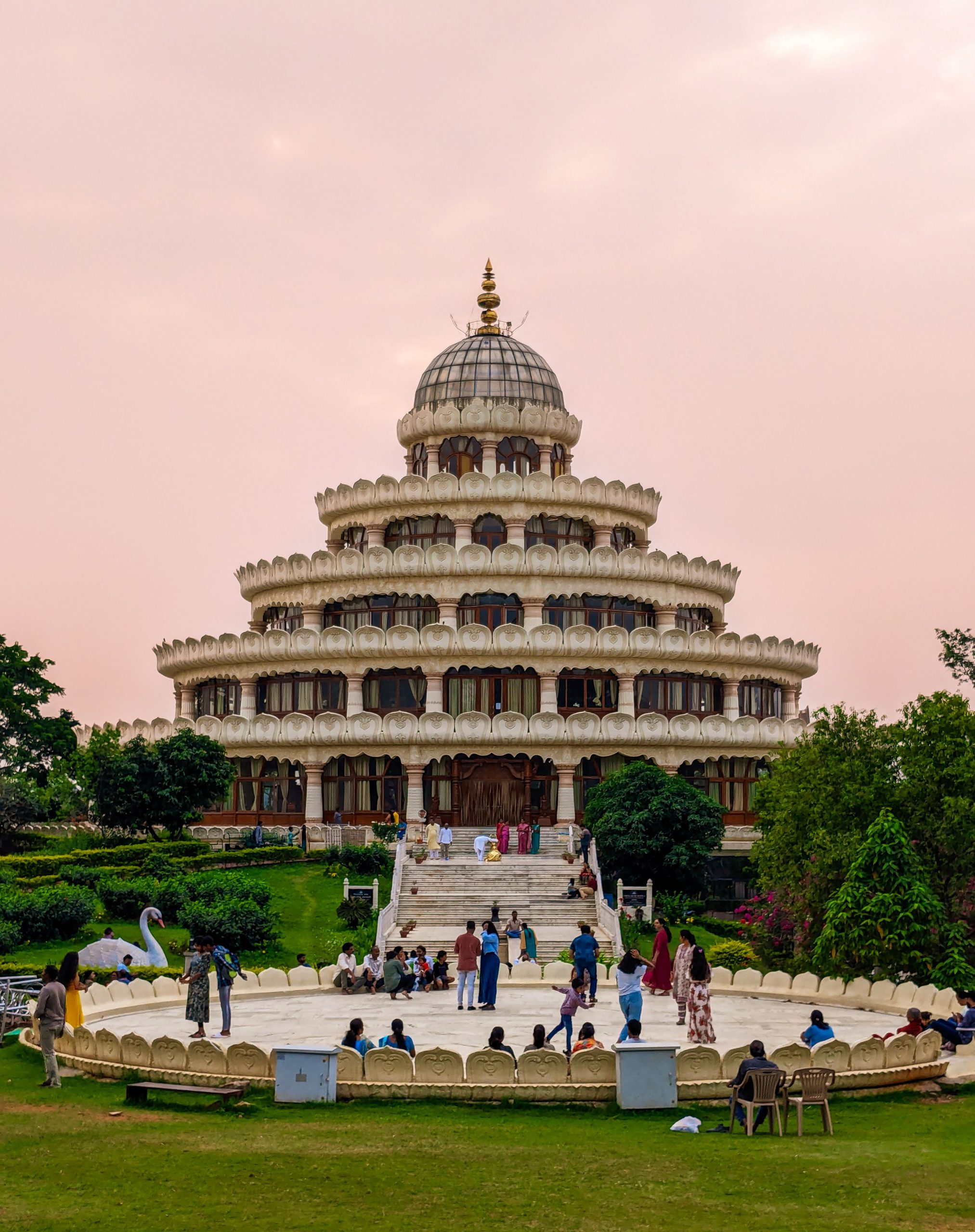 A stunning Indian monument surrounded by greenery and visitors in a park setting.